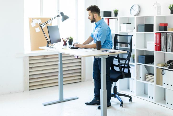 Un jeune homme debout dans le bureau et travaillant à la table de l’ordinateur